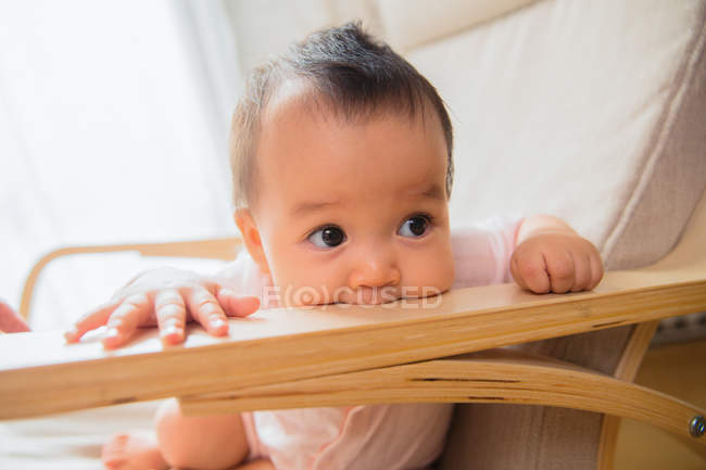 Крупный план младенца, сидящего на качающемся стульчике и отводящего взгляд от дома — стоковое фото