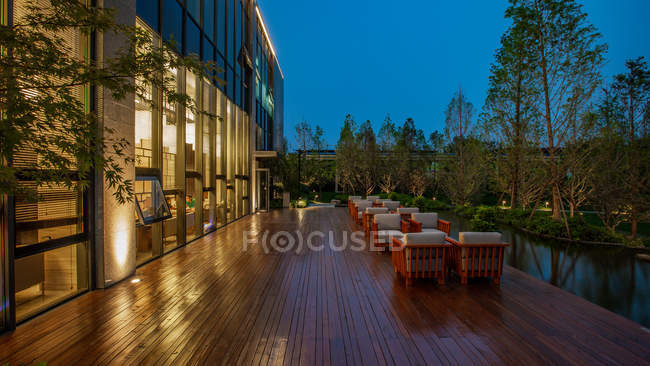 Modern building with illuminated windows and chairs on terrace in the evening — Stock Photo