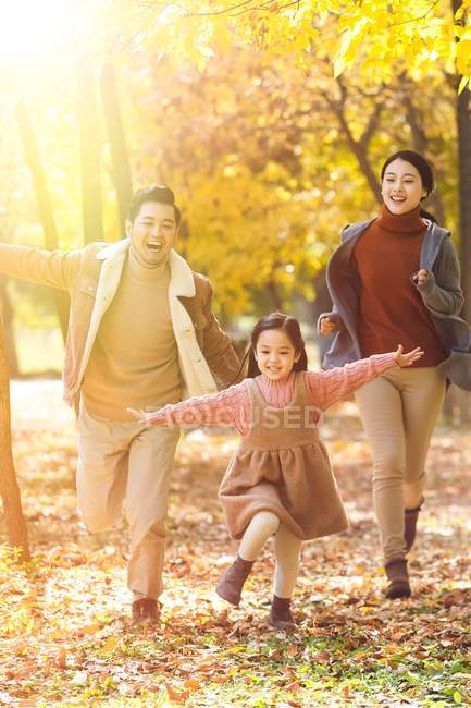 Felici genitori asiatici e figlia in esecuzione nel parco autunnale — Foto stock