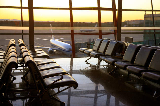 View of planes through window from empty airport lounge during sunset — Stock Photo