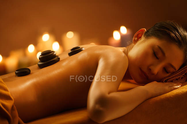 Bella giovane asiatico donna sdraiato su massaggio tavolo con pietre su indietro a spa — Foto stock