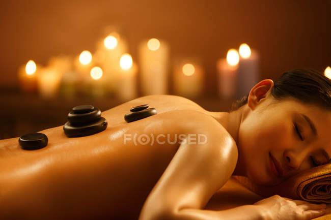 Beautiful young asian woman lying on massage table with stones on back at spa — Stock Photo