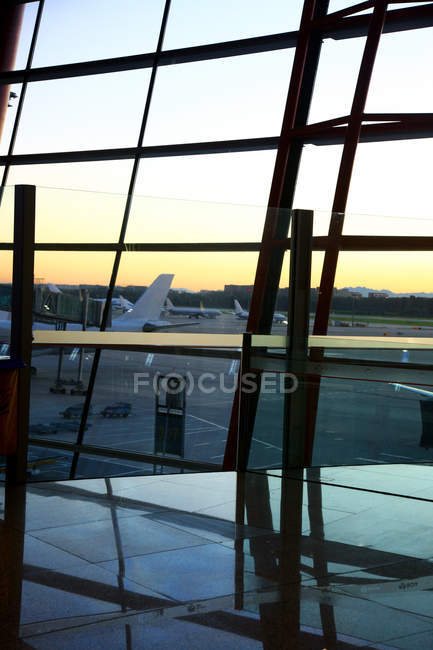 Blick auf Flugzeuge durch Fenster aus leerer Flughafenlounge bei Sonnenuntergang — Stockfoto