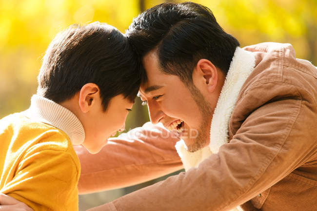 Seitenansicht glücklicher asiatischer Vater und Sohn, die sich im Herbstwald die Stirn berühren — Stockfoto