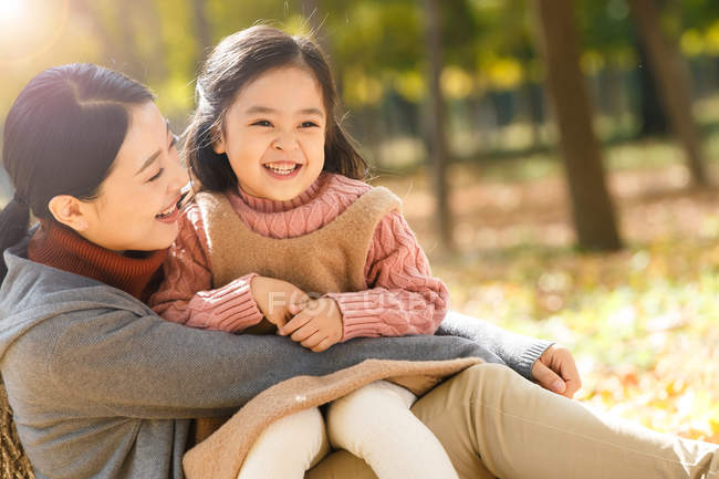 Happy asian mother and daughter sitting and hugging in autumn park — Stock Photo