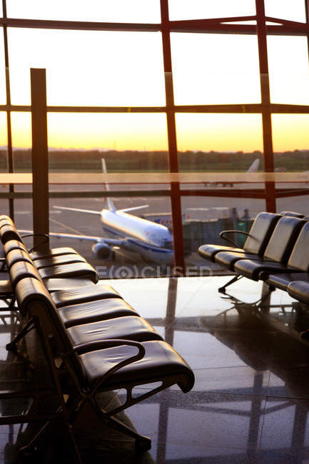 Vue des avions par la fenêtre depuis le salon vide de l'aéroport pendant le coucher du soleil — Photo de stock