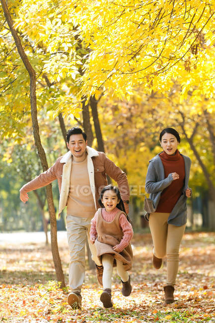 Счастливые азиатские родители и дочь, бегающие в осеннем парке — стоковое фото