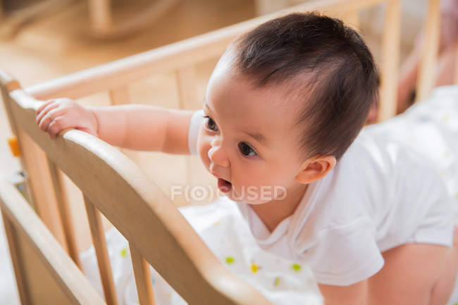 Überrascht kleines asiatisches Baby lehnt an Krippe und schaut zu Hause weg — Stockfoto