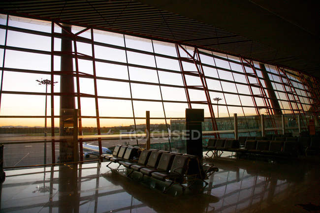 Vista de los aviones a través de la ventana desde el salón vacío del aeropuerto durante el atardecer - foto de stock