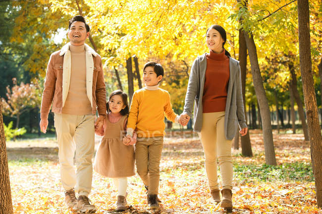 Feliz asiática familia con dos niños cogidos de la mano y caminando juntos en otoño parque - foto de stock