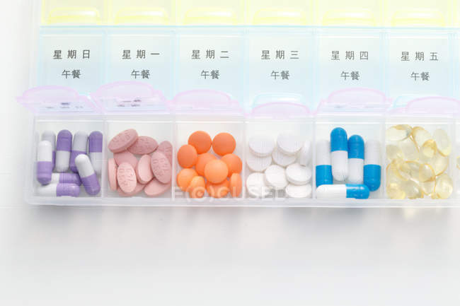 Vista dall'alto delle pillole nel contenitore giornaliero sulla superficie bianca — Foto stock