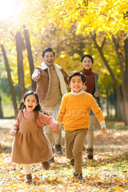 Happy young parents and cute kids running in autumn forest and smiling at camera — Stock Photo