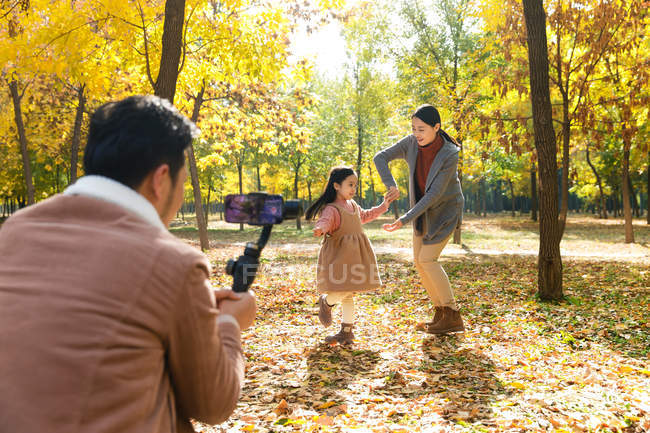 Heureux asiatique père prise de photo de fille et femme avec smartphone dans le parc automnal — Photo de stock