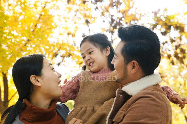 Low angle view of happy asian parents and daughter hugging in autumnal park — Stock Photo