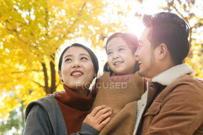 Faible angle de vue de heureux asiatiques parents et fille câlins dans le parc automnal — Photo de stock