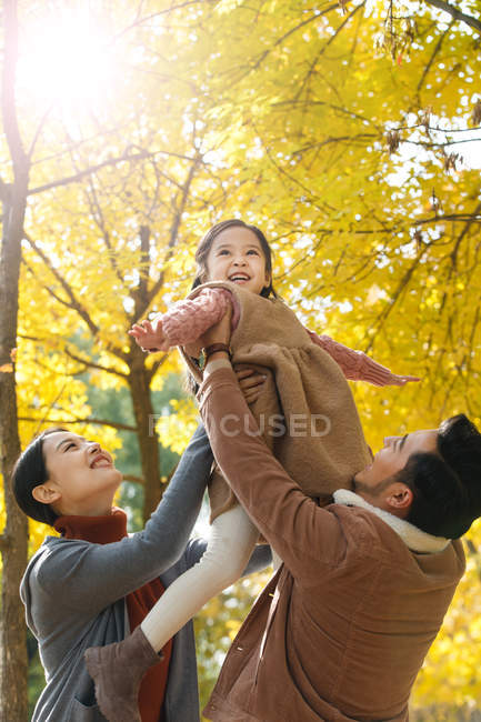 Glückliche asiatische Eltern heben Tochter in herbstlichen Park — Stockfoto