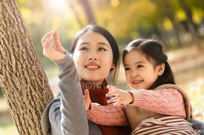 Feliz asiático madre y hija mirando el otoño hoja en parque - foto de stock