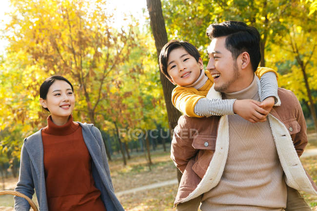 Happy asian father giving piggyback to son in autumnal park — Stock Photo