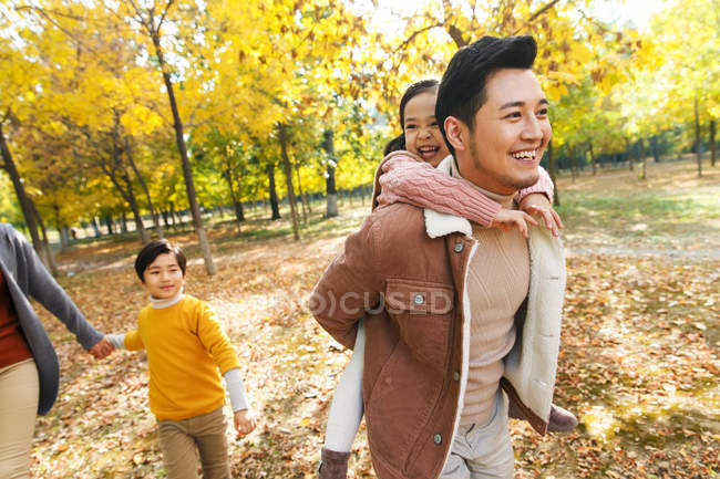 Feliz jovem pai piggybacking adorável pequena filha durante o descanso familiar no parque de outono — Fotografia de Stock