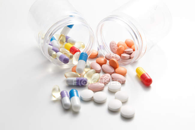 Scattered pills from jars on white surface — Stock Photo