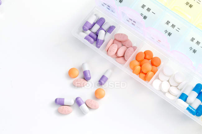Vue du dessus des pilules dans le récipient quotidien sur la surface blanche — Photo de stock