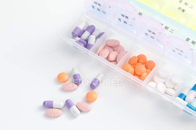 Vista de ángulo alto de píldoras en contenedor diario en la superficie blanca - foto de stock