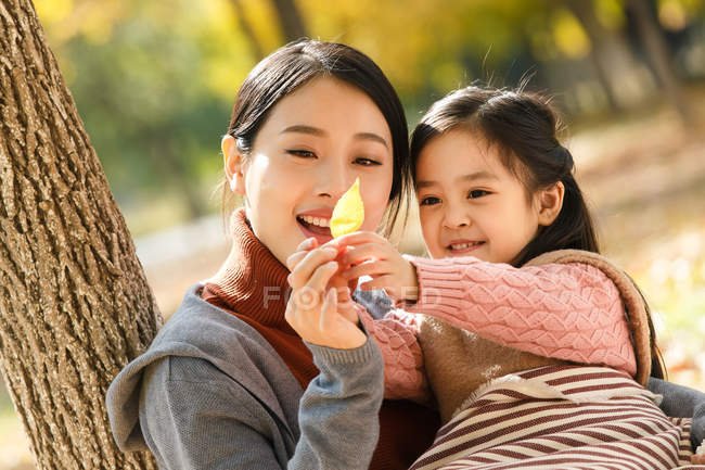 Happy asian mother and daughter looking at autumn leaf in park — Stock Photo