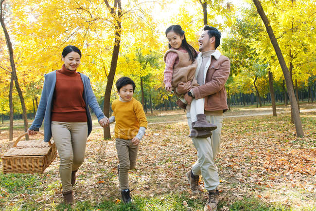 Happy young asian family with picnic basket walking in autumn park — Stock Photo