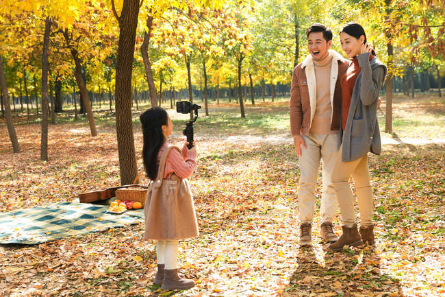 Happy asian daughter taking photo of parents with smartphone in autumnal park — Stock Photo