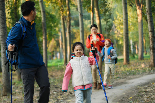 Happy young asian family with backpacks and trekking sticks walking together in forest — Stock Photo