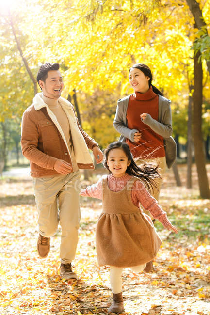 Счастливые азиатские родители и дочь, бегающие в осеннем парке — стоковое фото