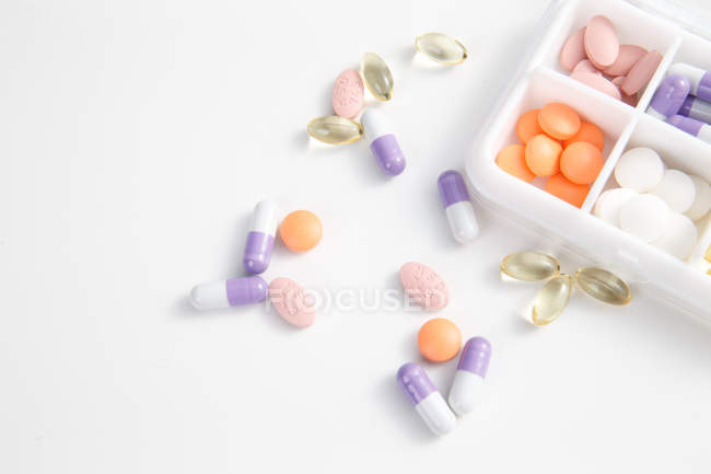 Vue grand angle des pilules dans le récipient quotidien sur la surface blanche — Photo de stock
