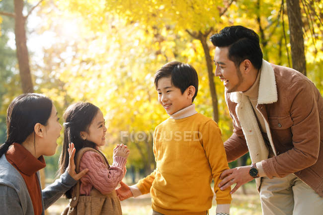 Счастливые молодые азиатские родители смотрят на очаровательных улыбающихся детей в осеннем лесу — стоковое фото