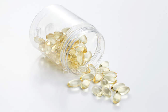 Pílulas dispersas de frasco na superfície branca — Fotografia de Stock