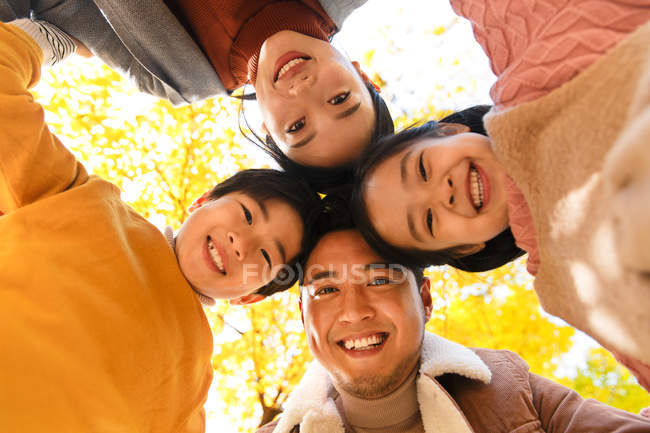 Blick von unten auf eine glückliche junge asiatische Familie mit zwei Kindern, die zusammen stehen und im herbstlichen Wald in die Kamera lächeln — Stockfoto