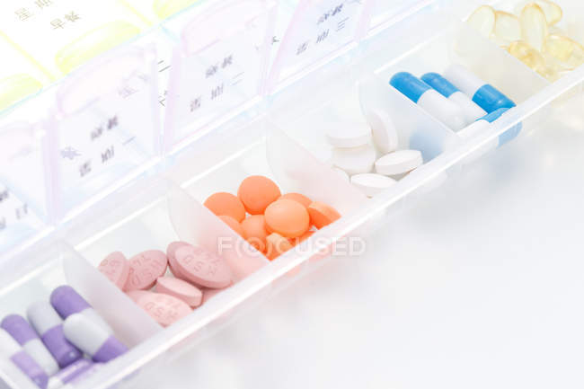 Vista de ángulo alto de píldoras en contenedor diario en la superficie blanca - foto de stock