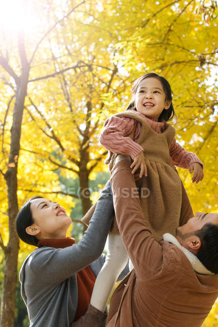 Happy asian parents lifting daughter in autumnal park — Stock Photo