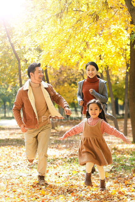 Happy asian parents and daughter running in autumnal park — Stock Photo