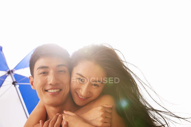 Happy asian boyfriend giving piggyback to girlfriend on beach — Stock Photo