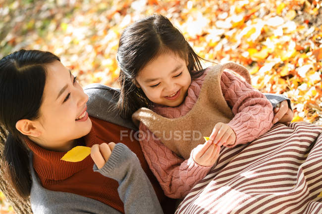 High angle view of beautiful happy asian mother and daughter playing with autumn leaves in park — Stock Photo