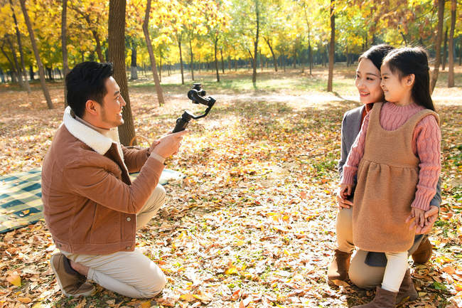Heureux asiatique père prise de photo de fille et femme avec smartphone dans le parc automnal — Photo de stock