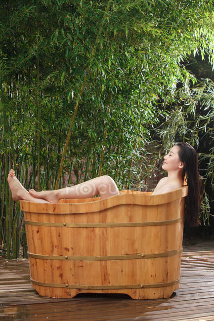 Hermosa mujer asiática acostada en bañera de madera en el jardín - foto de stock