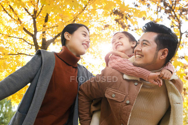 Bajo ángulo vista de feliz asiático padre dando piggyback a hija en otoñal parque - foto de stock