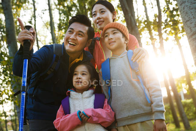 Low angle view of happy family with backpacks trekking and looking away together in autumn forest — Stock Photo