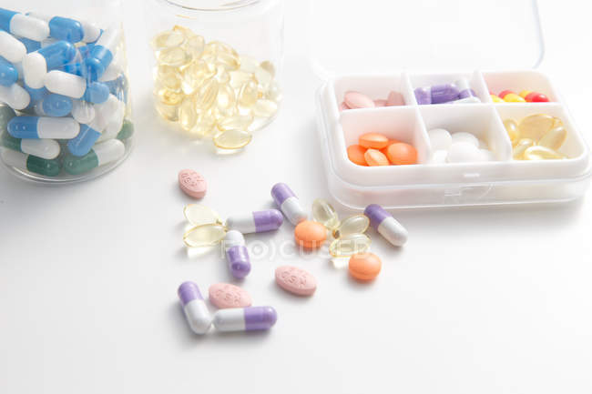 Vue grand angle des pilules dans le récipient quotidien sur la surface blanche — Photo de stock