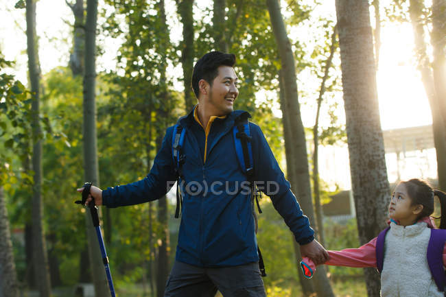 Feliz padre e hija tomados de la mano y caminando en el parque otoñal - foto de stock