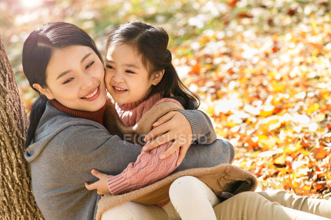 Alto ángulo vista de feliz asiático madre y hija sentado y abrazando en otoño parque - foto de stock