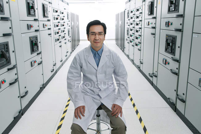 Технический персонал в белом халате улыбается в камеру во время работы в комнате напряжения — стоковое фото