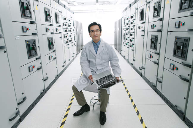 Technical personnel in white coat working with laptop computer in the voltage room — Stock Photo