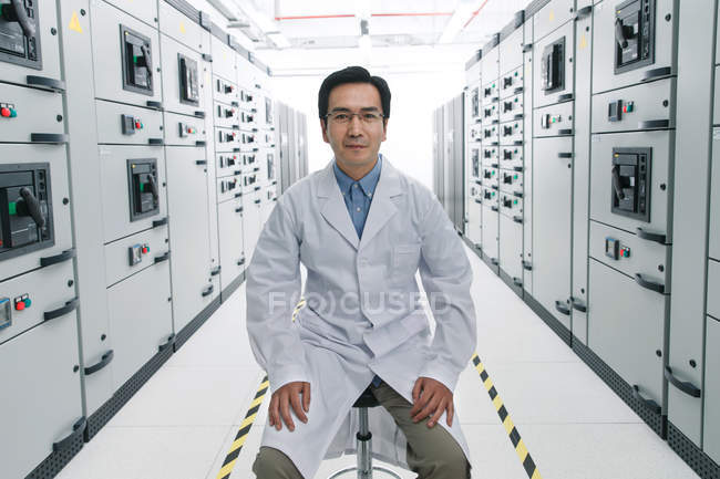 Personal técnico en bata de laboratorio sonriendo a la cámara mientras trabaja en la sala de voltaje - foto de stock